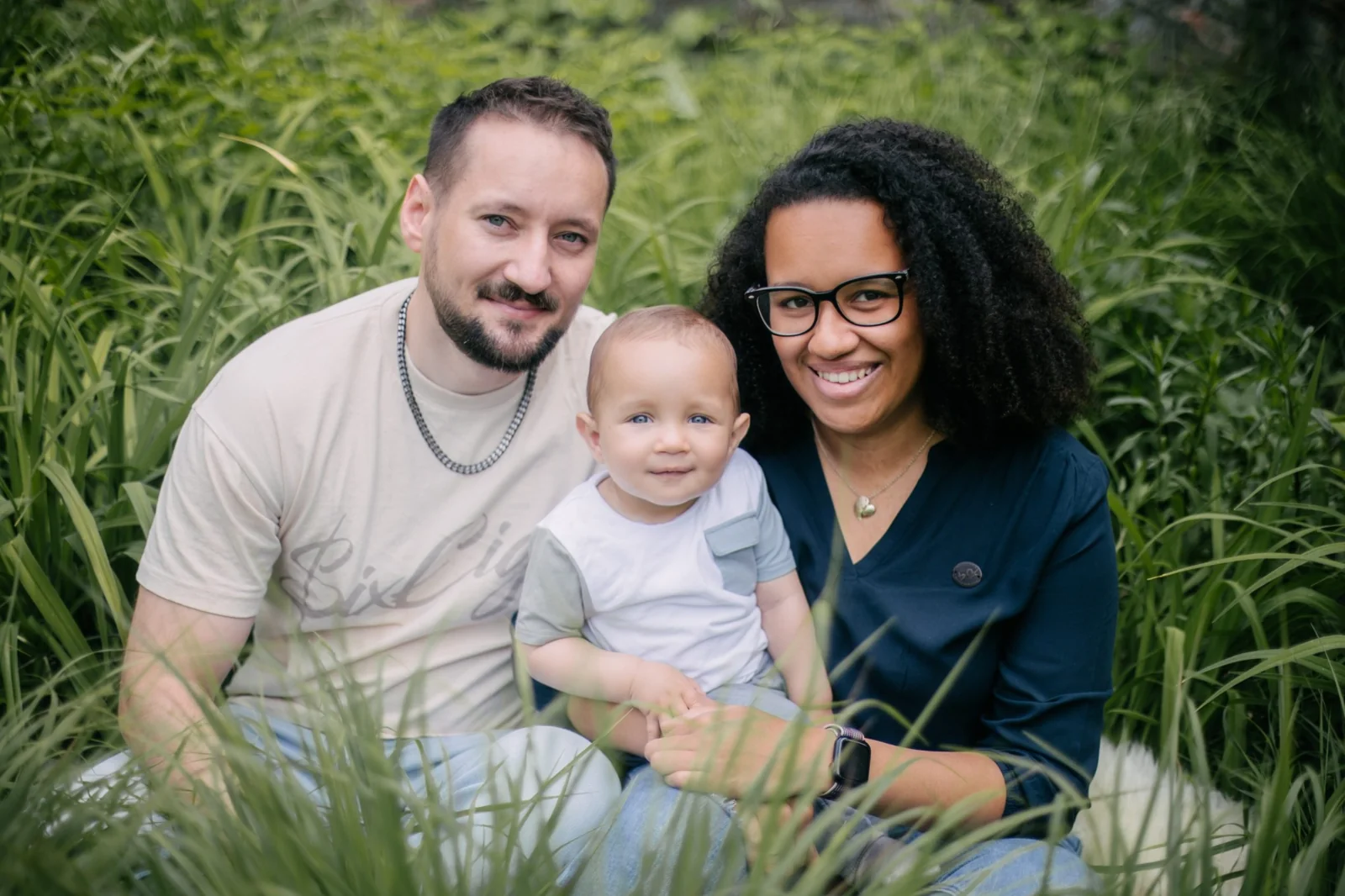 Eltern sitzen mit ihrem Kleinkind in einer grünen Wiese