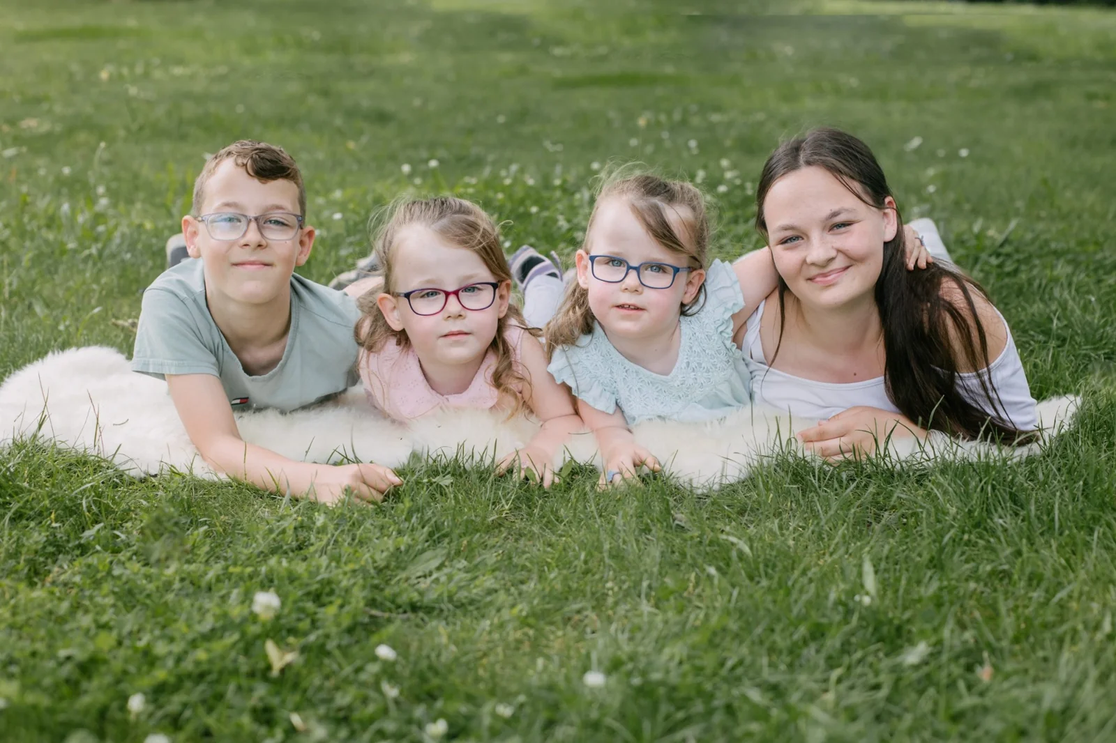 Vier Kinder liegen nebeneinander auf einer Decke im Gras