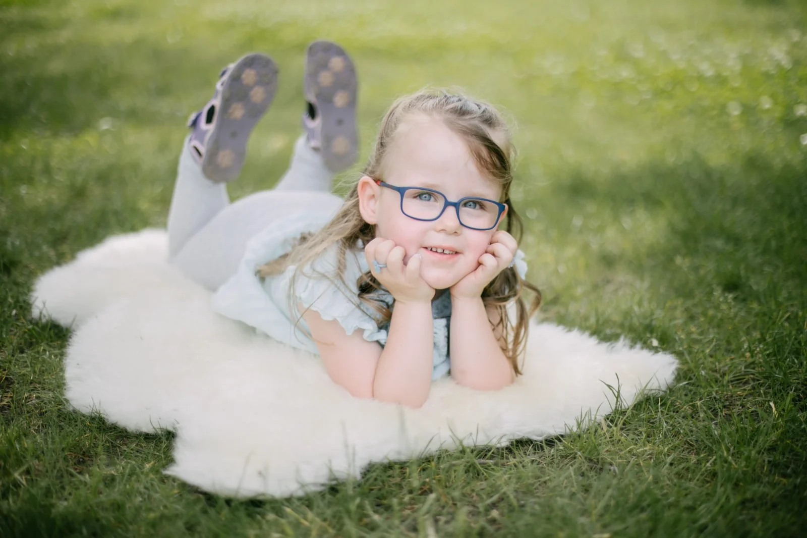 Kind mit blauer Brille liegt auf einer hellen Decke im Gras