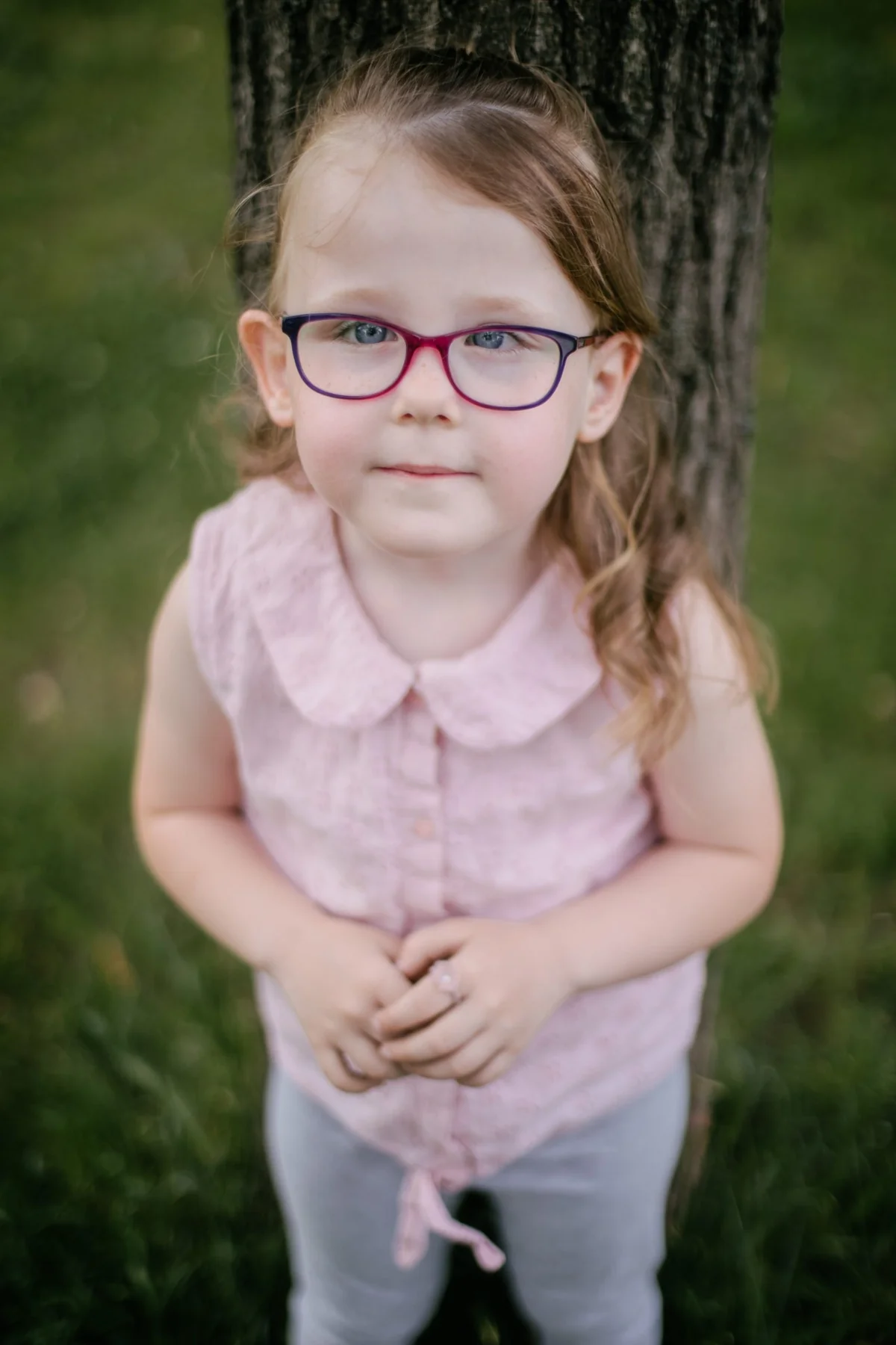 Kind mit violetter Brille vor einem Baum