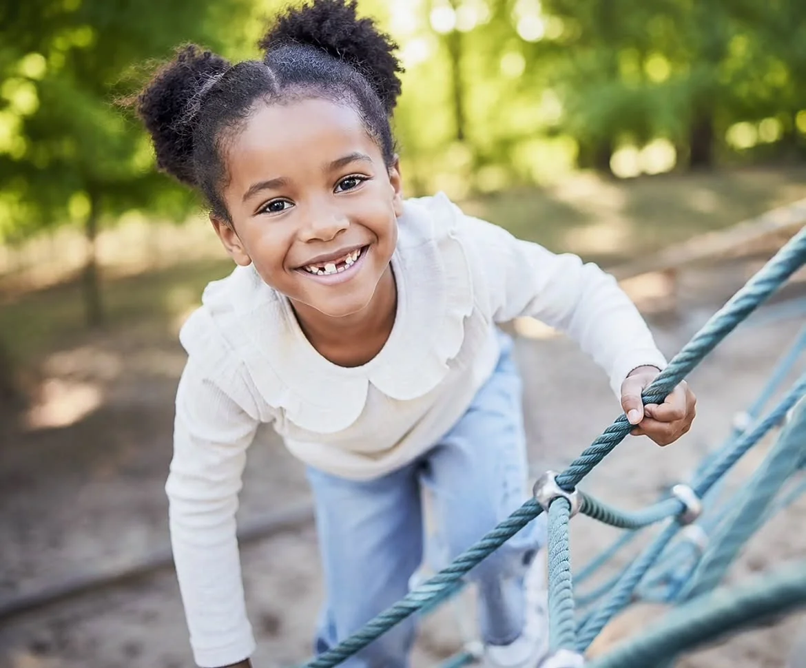 Kind lacht beim Klettern am Seil auf dem Spielplatz