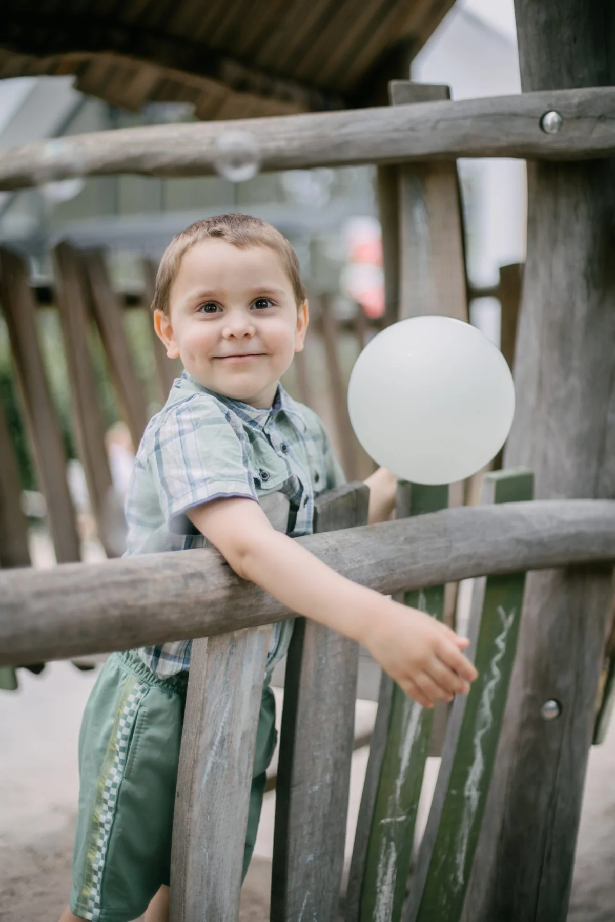 Kind mit weißem Luftballon auf einem Holzspielgerät